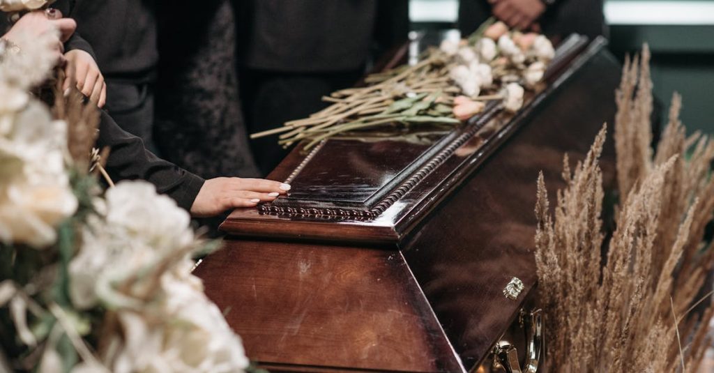 A poignant funeral moment with mourners gathered around a coffin decorated with flowers.